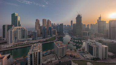 Dubai Marina with boats and yachts parked in harbor and skyscrapers around canal aerial  during all day from sunrise. Shadows moving fast. Towers of JBR district on a background