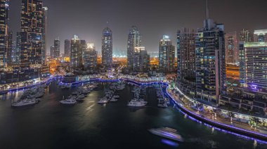 Panorama showing luxury yacht bay in the city aerial night  in Dubai marina. Modern skyscrapers along waterfront promenade and boats floating in harbor