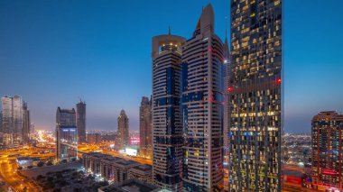 Aerial view of Dubai International Financial District with many skyscrapers day to night transition  after sunset. Traffic on a road junction near parking lot. Dubai, UAE.