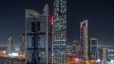 Panorama showing aerial view of Dubai International Financial District with many illuminated skyscrapers night . Traffic on a road near multi storey parkings. Dubai, UAE.