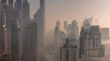 Dubai Marina 'nın en yüksek karşılama bloğundaki çeşitli gökdelenlerin suni kanallı gündoğumu sırasında görüntüsü. Birçok kule ve yat arasında sabah sisi