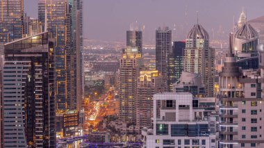 Dubai Marina and Media City districts with modern skyscrapers and office buildings aerial day to night transition . Traffic on overpass and road intersection near green park on a background