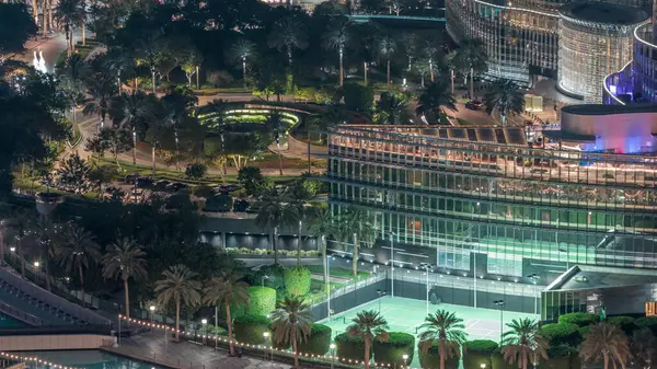 stock image Aerial view of park area with palms in Dubai downtown night . Sport fields near illuminated skyscrapers and towers from above with traffic on circle