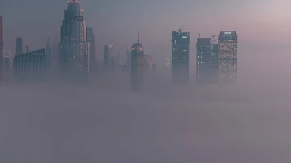 空中からの眺め朝の霧はドバイ国際金融センター地区の夜から昼への移行をカバーしました 日の出前に近代的な高層ビルがあるオフィスタワーとホテル — ストック写真