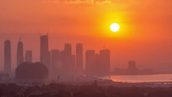 高層ビルやタワーが建設中のドバイクリークハーバーの日の出 ビルの後ろに大きな赤い太陽が昇る — ストック写真