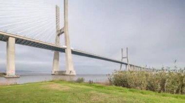 Architectural landmark Vasco da Gama Bridge over the Tagus River in Lisbon, Portugal. Green grass and cloudy sky. The longest bridge in the European Union.