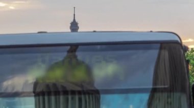 Güneş, arka planda Eyfel kulesi olan bir otobüs durağı ve trafik olan Paris Sufflot Caddesi 'ndeki bir binanın arkasında batıyor. Yaz gününde bulutlu turuncu gökyüzü