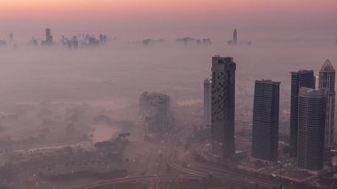 Big crossroad junction between JLT district and Dubai Marina intersected by Sheikh Zayed Road night to day transition aerial . Cars traffic covered by morning fog