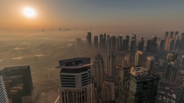 Panorama of Dubai Marina with JLT skyscrapers and golf course during sunrise , Dubai, United Arab Emirates. Aerial view from above towers foggy morning. City skyline with orange sky