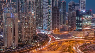 Skyscrapers of Dubai Marina with illuminated highest residential buildings day to night  after sunset. Aerial top view from JLT district with highway intersection