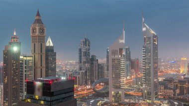 Skyscrapers on Sheikh Zayed Road and DIFC day to night transition  in Dubai, UAE. Towers in financial centre aerial view from above. Cloudy sky after sunset