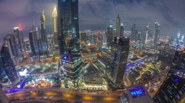 Panorama of futuristic skyscrapers after sunset in financial district business center in Dubai with traffic on a road day to night transition . Aerial view from above with cloudy sky