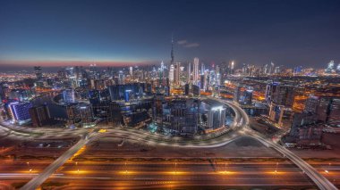 Panoramic skyline of Dubai with business bay and downtown district day to night . Aerial view of many modern skyscrapers with traffic on al khail road after sunset. United Arab Emirates.