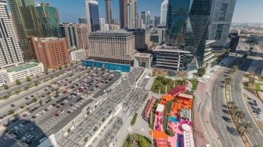 Dubai Uluslararası Finans Bölgesi ve büyük otopark anteni. Panoramik iş manzarası ve gölgeli finans kuleleri. Şehir merkezine yakın otelleri ve alışveriş merkezleri olan gökdelenler.