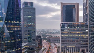 Dubai International Financial district night to day transition . Aerial view of business office towers before sunrise. Illuminated skyscrapers with road traffic and Deira district on a background