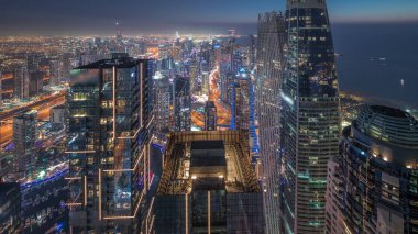 Skyline panoramic view of Dubai Marina showing canal surrounded by illuminated skyscrapers along shoreline aerial day to night transition . Floating yachts and boats after sunset. DUBAI, UAE