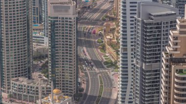 Yukarıdan JBR ve Dubai Marina gökdelenlerinin ve lüks binaların havadan görüntüsü. Uzun gölgeli modern kuleler sabah ve yol trafiğinde hızla ilerliyor.
