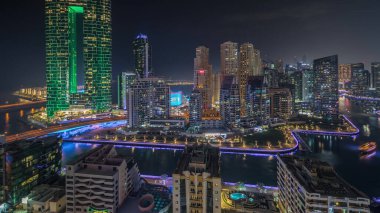 Panorama showing Dubai Marina skyscrapers and JBR district with luxury buildings and resorts aerial night . Illuminated waterfront and boats floating in canal