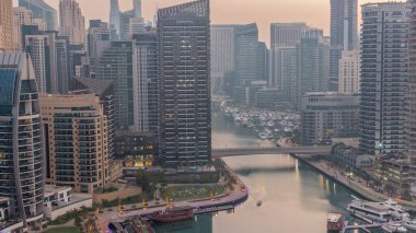 Dubai Marina with boats and yachts parked in harbor and illuminated skyscrapers around canal aerial night to day transition  before sunrise. Towers along waterfront