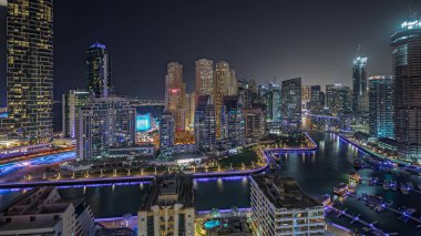 Panorama showing Dubai Marina with several boat and yachts parked in harbor and illuminated skyscrapers around canal aerial night . Towers of JBR district on a background