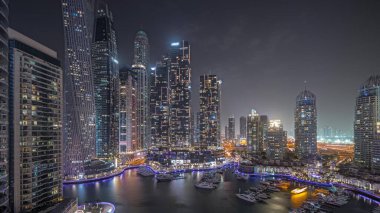 Panorama showing Dubai marina tallest skyscrapers and yachts in harbor aerial night . View at apartment buildings, hotels and office blocks, modern residential development of UAE