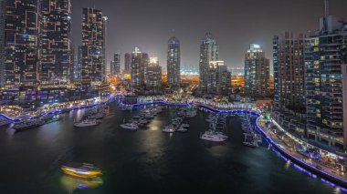 Panorama showing luxury yacht bay in the city aerial night  in Dubai marina. Modern skyscrapers along waterfront promenade and boats floating in harbor