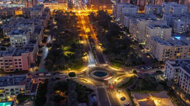 Low rise buildings in Greens district aerial day to night transition . Dubai skyline with palms and trees. Traffic on a road intersection