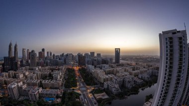 Skyscrapers in Barsha Heights district and low rise buildings in Greens district aerial night to day transition  panorama. Dubai skyline with palms and trees