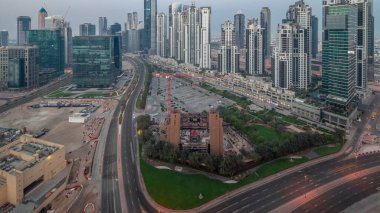 Bay Avenue with modern towers residential development in Business Bay aerial panoramic night to day transition , Dubai, UAE. Skyscrapers with traffic on a road near big parking lot