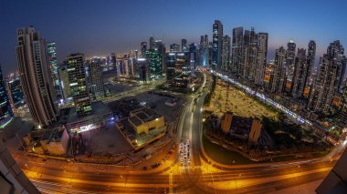 Panoramic skyline of Bay Avenue with modern towers residential development in Business Bay aerial day to night transition , Dubai, UAE. Skyscrapers with traffic on a road near big parking lot