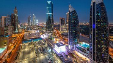 Aerial panoramic view of Dubai International Financial District with many skyscrapers night after sunset. Traffic on a road near parking lot at shopping avenue walking area. Dubai, UAE.