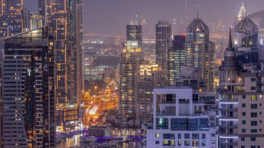 Dubai Marina and Media City districts with modern skyscrapers and office buildings aerial day to night transition . Traffic on overpass and road intersection near green park on a background