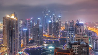 View of various skyscrapers in tallest recidential block in Dubai Marina aerial during all night  with artificial canal. Many towers with blinking lights and yachts. Cloudy sky