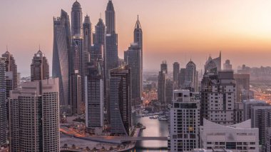 View of various skyscrapers in tallest recidential block in Dubai Marina aerial night to day transition  with artificial canal. Many towers and yachts before sunrise