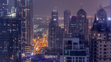 Dubai Marina ve Media City semtleri modern gökdelenler ve ofis binaları ile tüm gece boyunca. Üstgeçitte trafik ve ışıkların kapandığı kavşak.