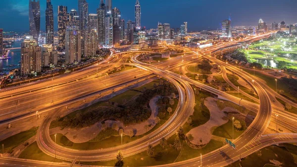 stock image Panorama of Dubai Marina highway intersection spaghetti junction day to night transition . Illuminated tallest skyscrapers after sunset and golf club on a background. Aerial top view from JLT district