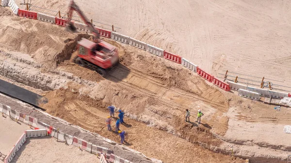 建設現場の航空機のクローズアップビューでの労働者と赤い掘削機掘り排水のグループ 修理中のパイプ — ストック写真