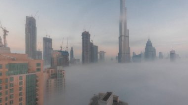 Sabahın erken saatlerinde, sisli bir gecede Dubai şehrinin hava görüntüsü. Gökdelenleri ve inşa halindeki kuleleri olan gelecekçi şehir gökdelenleri