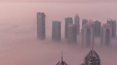 Şeyh Zayed Yolu yakınlarındaki JLT gökdelenleri gece gündüz geçiş yapıyor. Aydınlanmış konut binaları ve kavşaktaki trafik. Güneş doğmadan önce sisli bir sabah