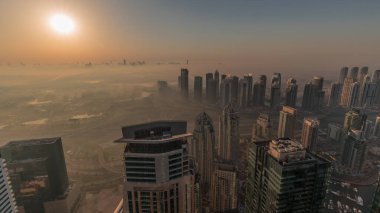 Panorama of Dubai Marina with JLT skyscrapers and golf course during sunrise , Dubai, United Arab Emirates. Aerial view from above towers foggy morning. City skyline with orange sky