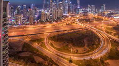 Panorama of Dubai Marina highway intersection spaghetti junction day to night transition . Illuminated tallest skyscrapers on a background. Aerial top view from JLT district after sunset