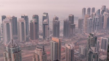 JLT skyscrapers and marina towers near Sheikh Zayed Road aerial night to day transition . Illuminated residential buildings and skyline with villas. Foggy morning before sunrise