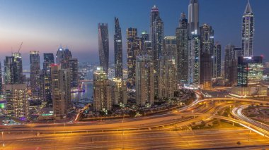 Dubai Marina 'nın gökdelenleri, gün batımından sonra gün batımından sonra karayolu trafiğiyle aydınlık konutlu binalar. JLT bölgesinden hava üst görünümü