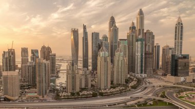 Dubai Marina highway intersection spaghetti junction evening . Tallest skyscrapers with reflection of sun on a glass surface. Aerial top view from JLT district during sunset with cloudy orange sky