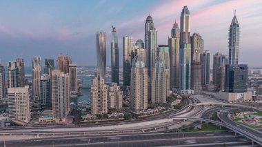 Dubai Marina highway intersection spaghetti junction night to day transition . Illuminated tallest skyscrapers on a background. Aerial top view from JLT district before sunrise