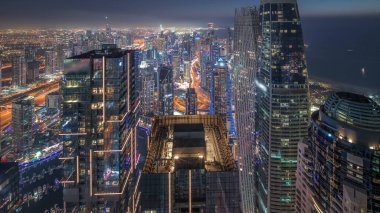 Skyline panoramic view of Dubai Marina showing canal surrounded by illuminated skyscrapers along shoreline aerial day to night transition . Floating yachts and boats after sunset. DUBAI, UAE