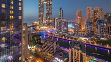 Günbatımından sonra Dubai Marina gökdelenleri ve JBR bölgesi aydınlık lüks binalar ve gece geçişleriyle dolu tatil beldeleri. Palmiyeler ve kanalda yüzen teknelerle dolu bir liman.