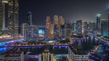 Panorama showing Dubai Marina with several boat and yachts parked in harbor and illuminated skyscrapers around canal aerial night . Towers of JBR district on a background