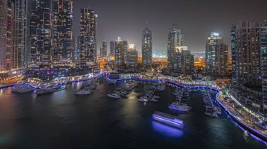 Panorama showing luxury yacht bay in the city aerial night  in Dubai marina. Modern skyscrapers along waterfront promenade and boats floating in harbor
