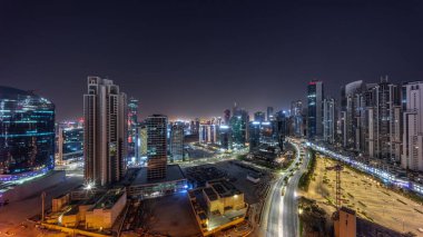 Dubai, BAE 'de gece boyunca Business Bay havacılık panoramik binasında aydınlatılmış modern kuleleri olan su kanalı. Yolunda trafik olan ve ışıkları kapanan gökdelenler.